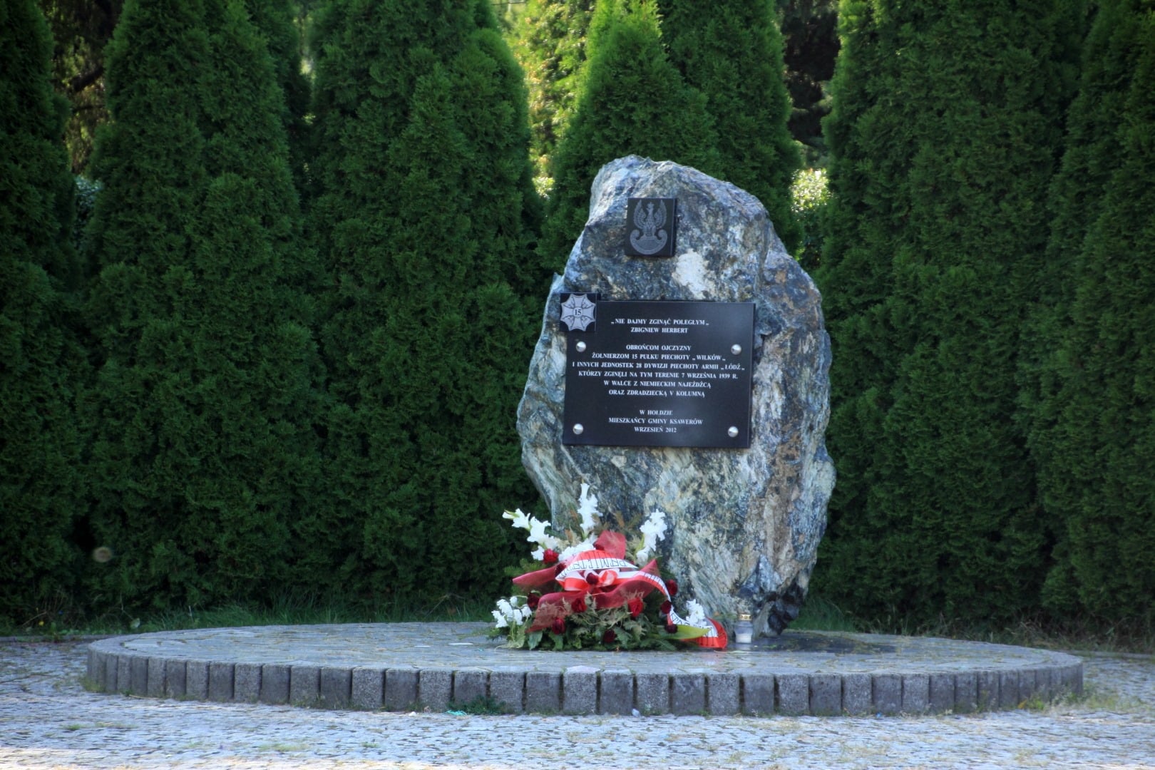 obelisk Zdjęcie przedstawia obelisk (kamień) przed którym znajduje się wieniec biało czerwonych kwiatów