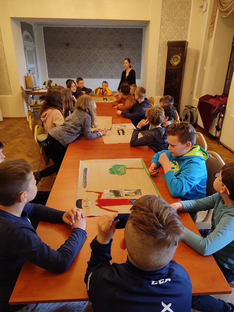 projekt dzieci siedzące przy stolikach, przed nimi znajdują się kartony z pracami